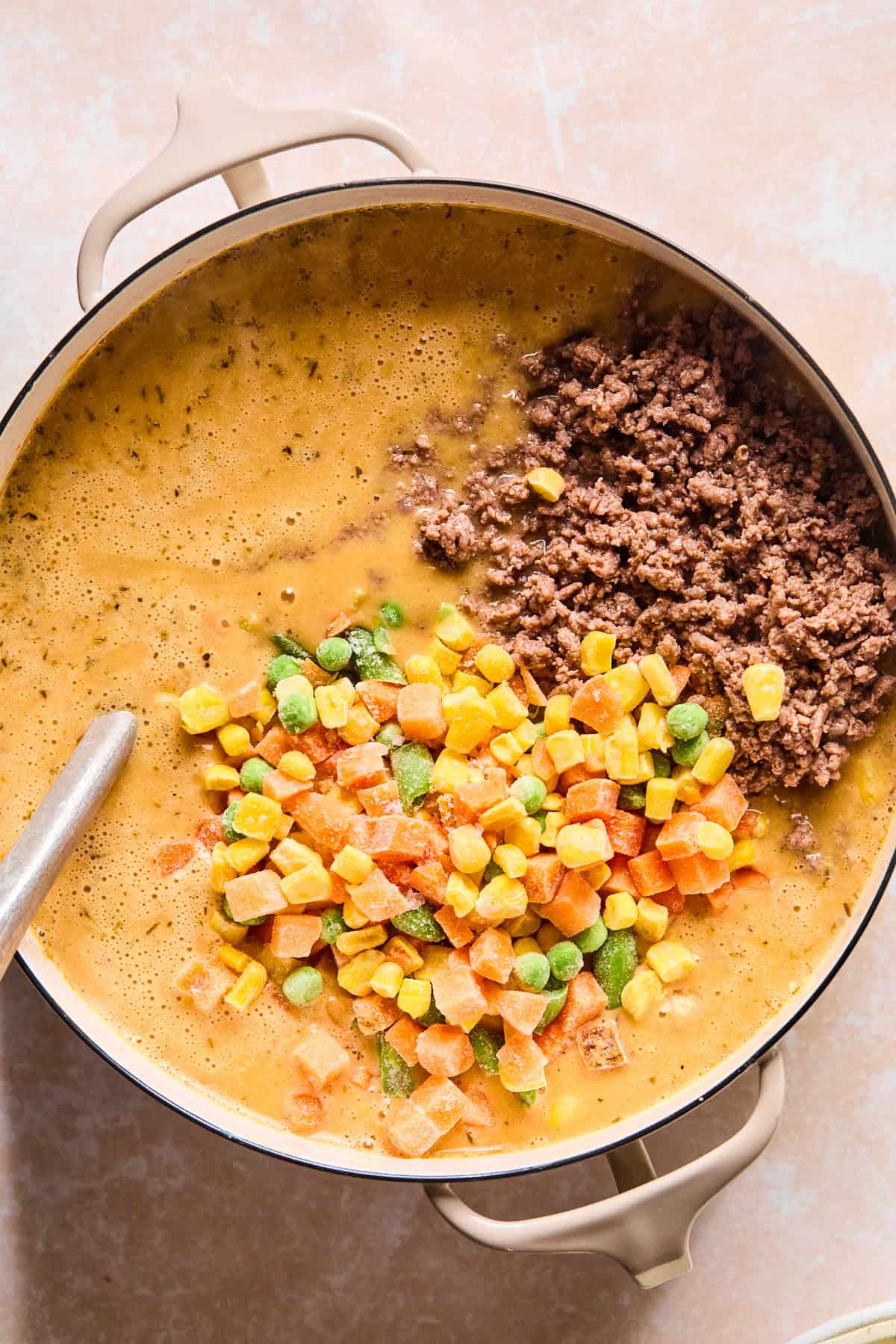Stirring cooked ground beef and frozen vegetables into shepherd's pie soup.