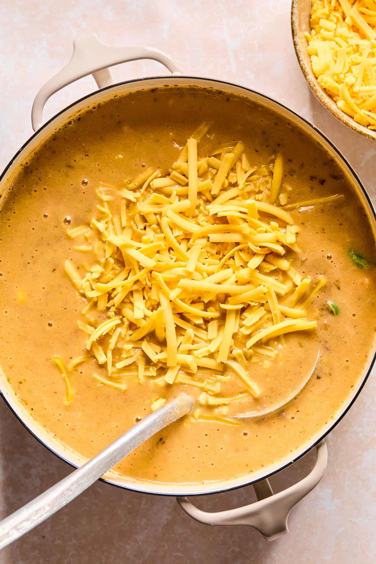 Shredded cheese being stirred into the soup with a ladle.