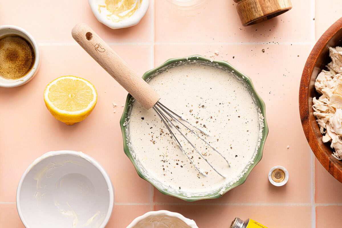 homemade caesar dressing in a bowl with a whisk surrounded by ingredients