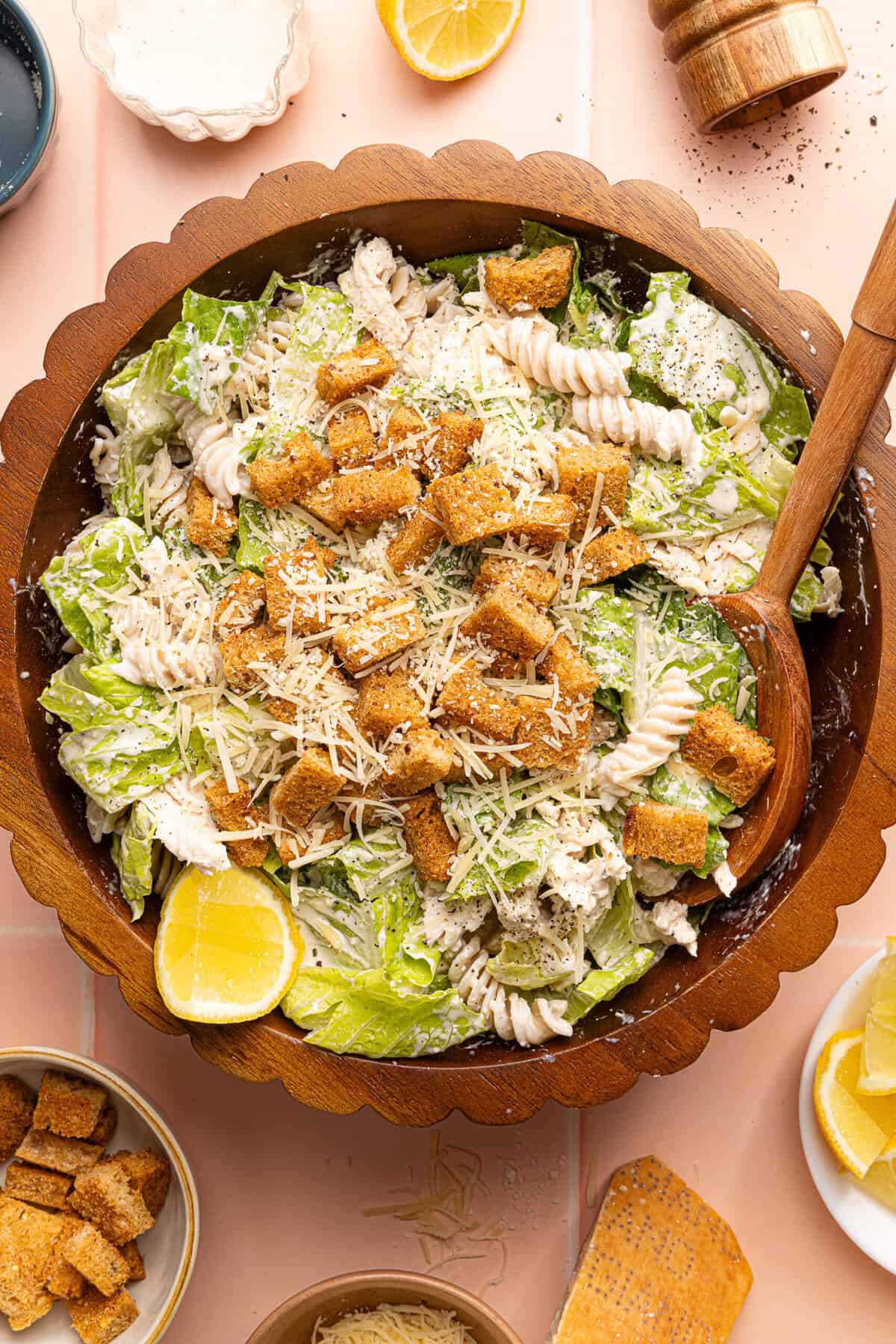 chicken caesar pasta salad topped with croutons in a wooden bowl