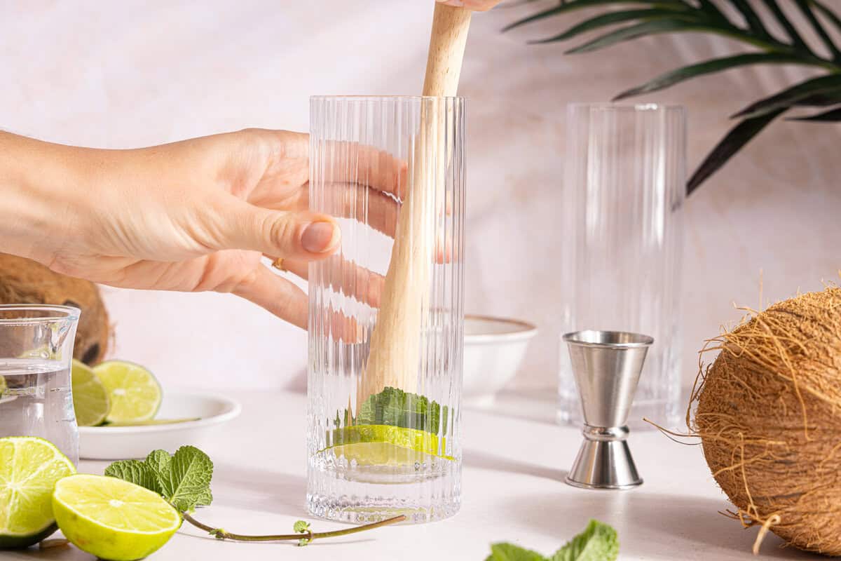 a lime wedge being muddled in a glass