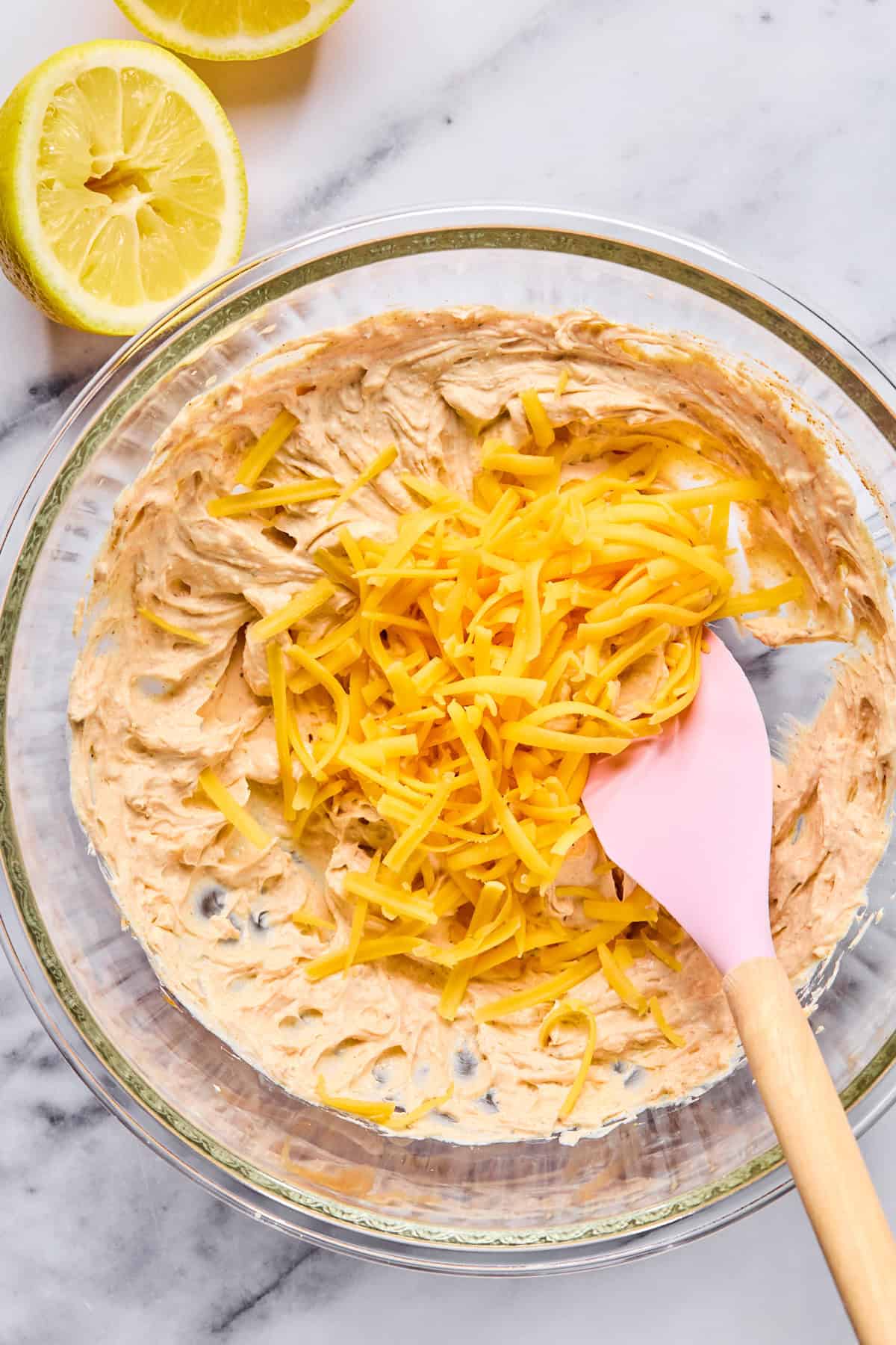 Shredded cheddar cheese being folded into the creamy crab dip mixture.