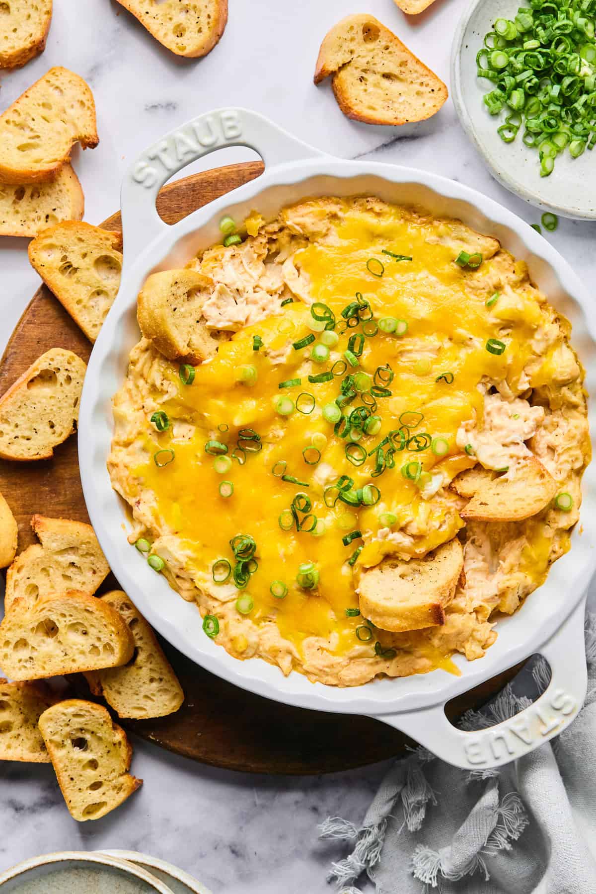 Hot crab dip in a baking dish garnished with green onions, with baguette slices in the dip and served around the dish.