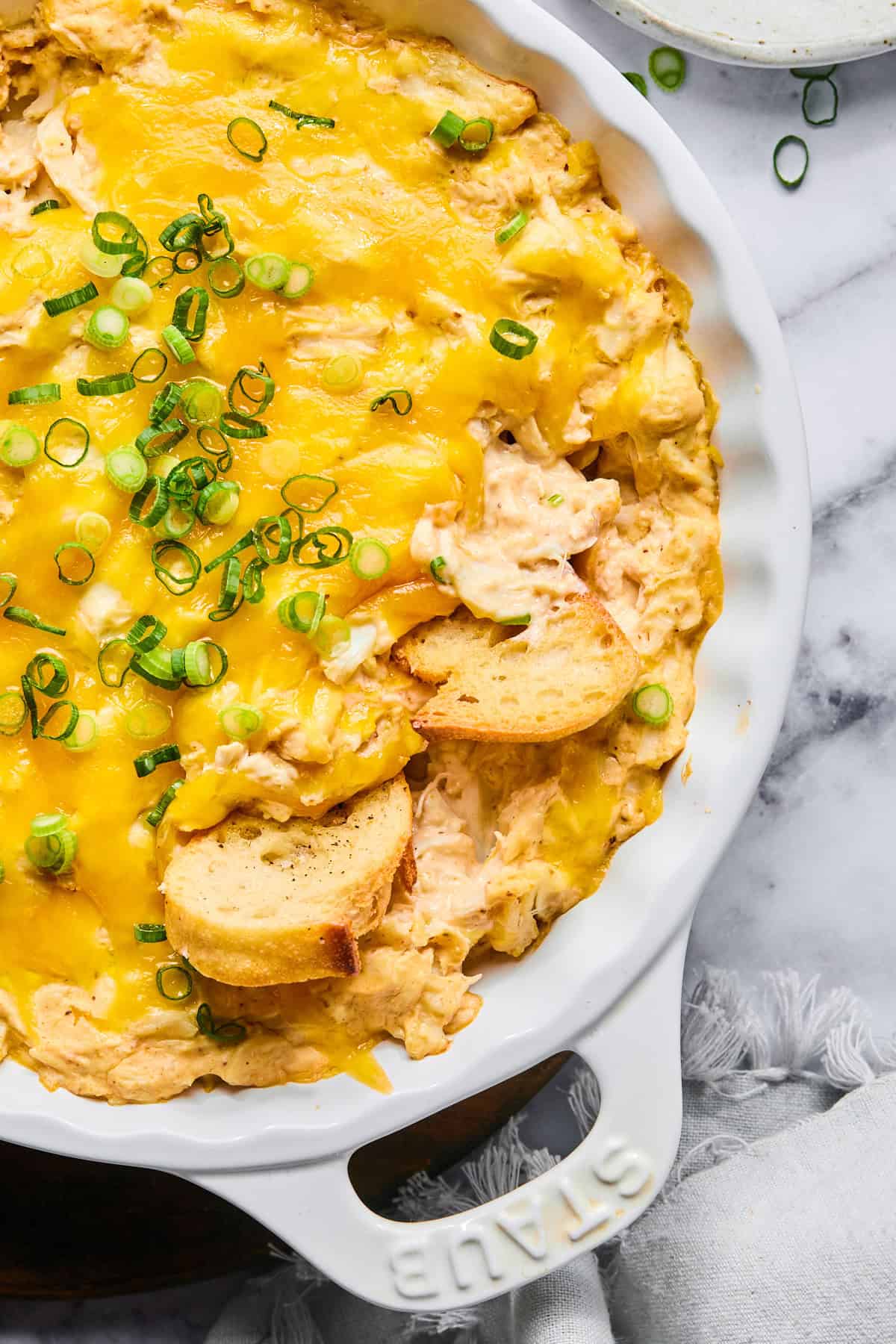 Close-up of hot crab dip in a baking dish garnished with green onions and served with baguette slices.