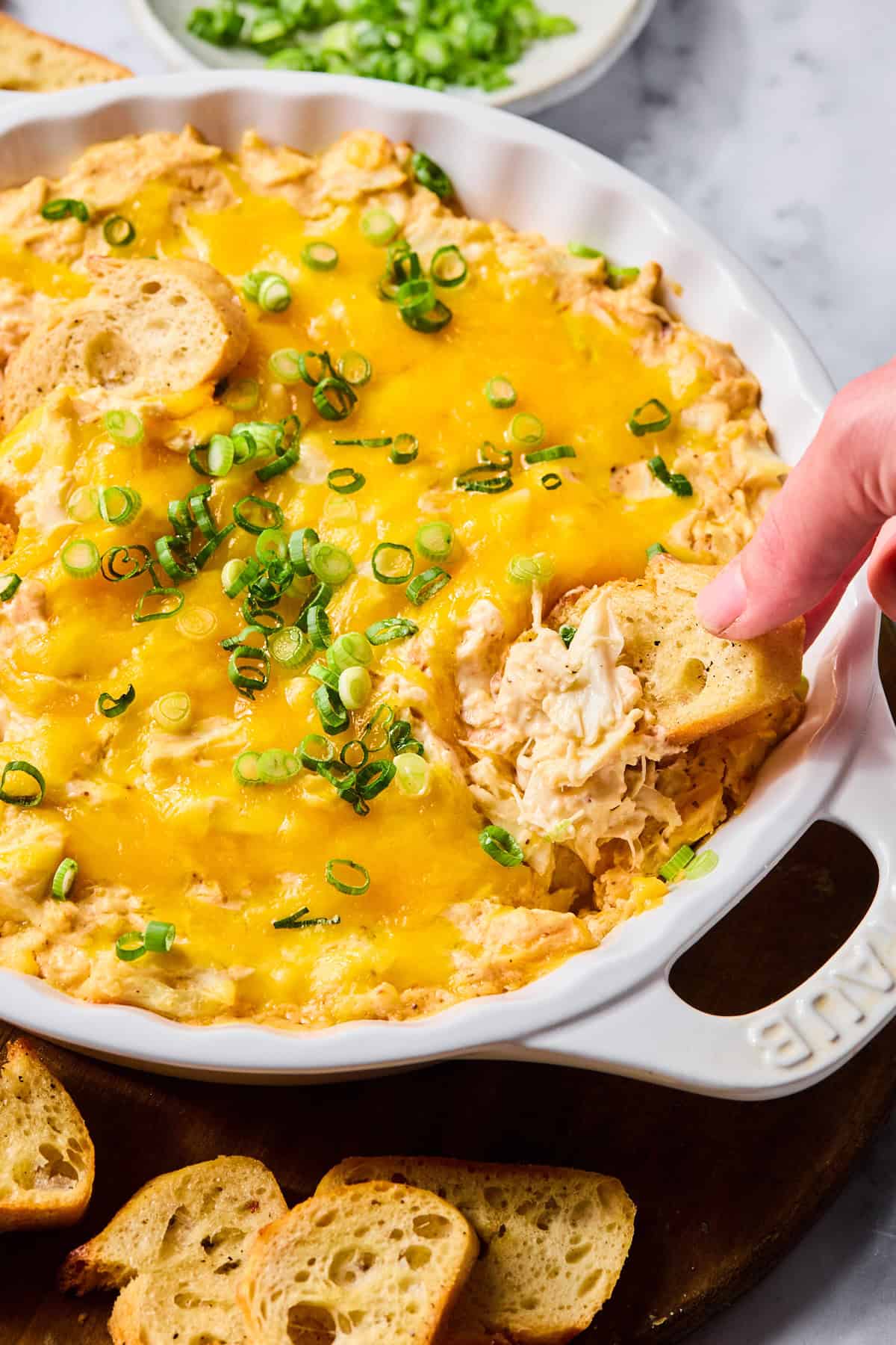 Baguette slice being dipped into warm, creamy crab dip.