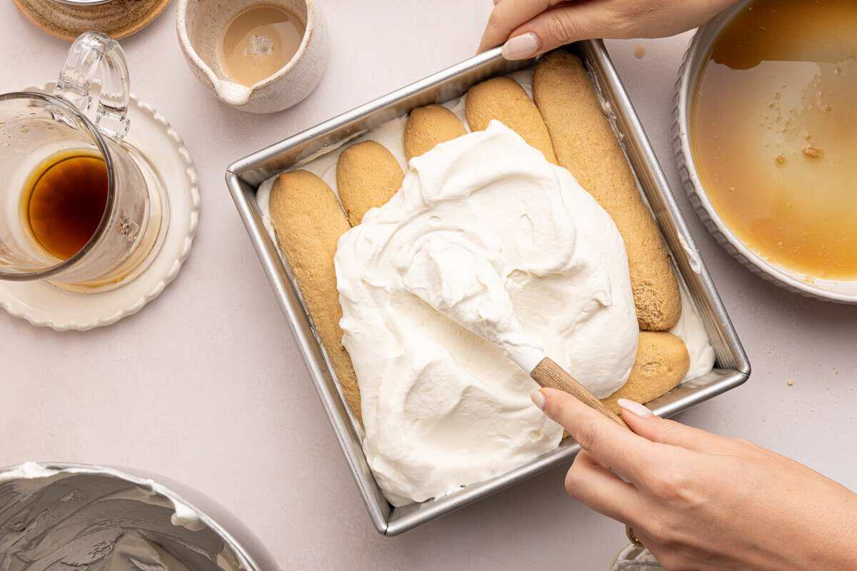 whipped cream being spread on lady fingers in a baking pan