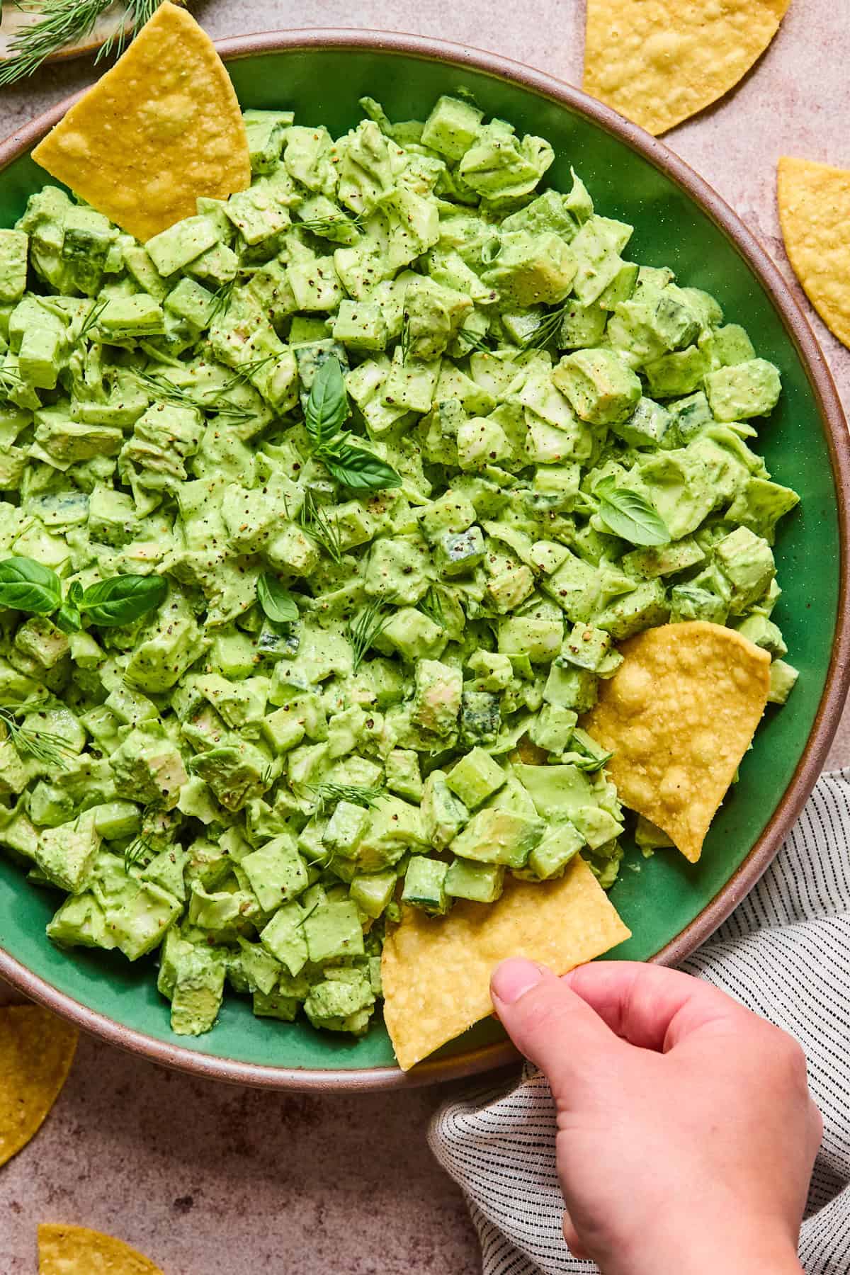 a hand dipping a chip into green chicken salad