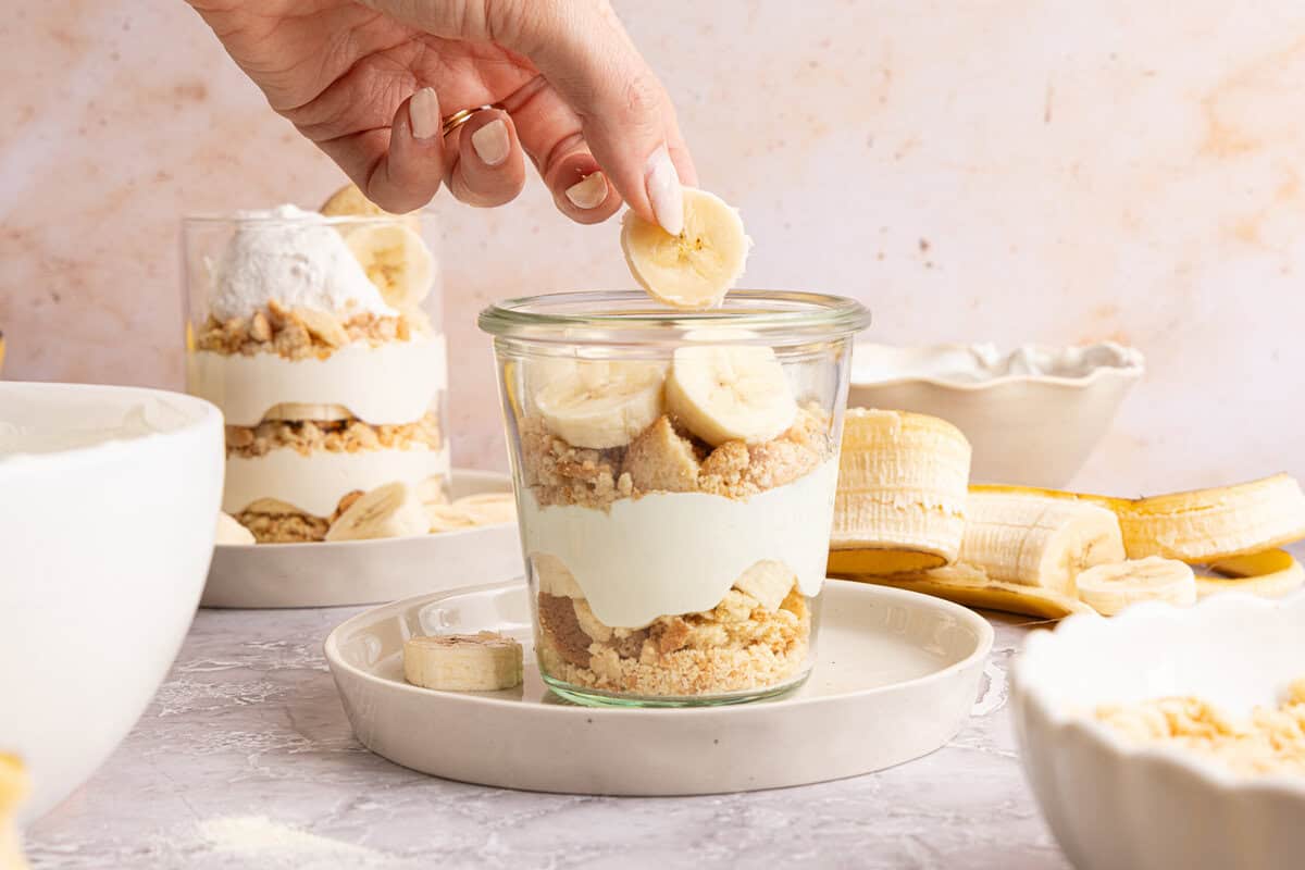 a hand adding ingredients to layers of banana pudding in a cup