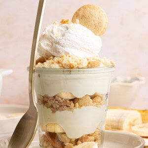 a banana pudding cup with a spoon rested against the side on a plate