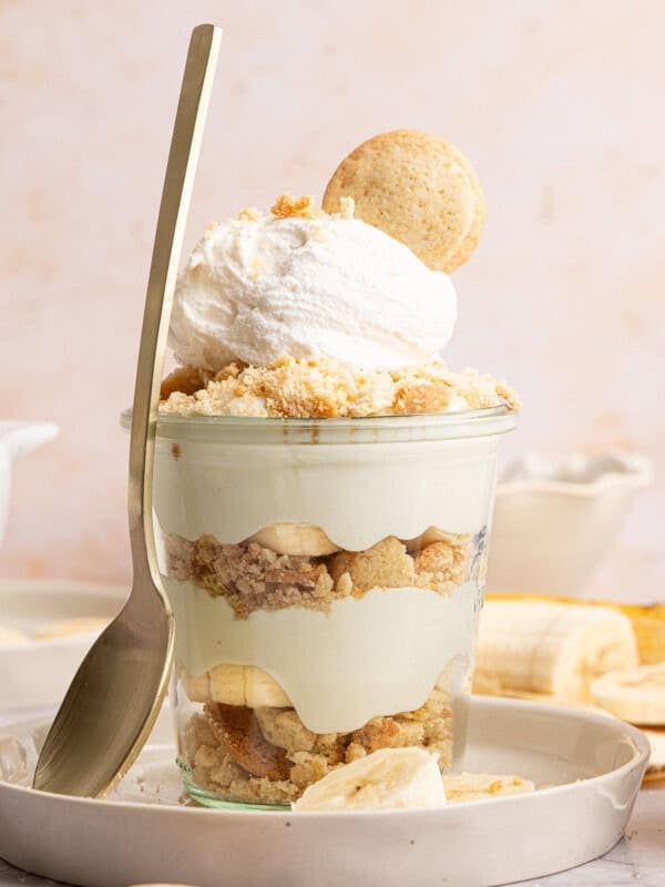 a banana pudding cup with a spoon rested against the side on a plate