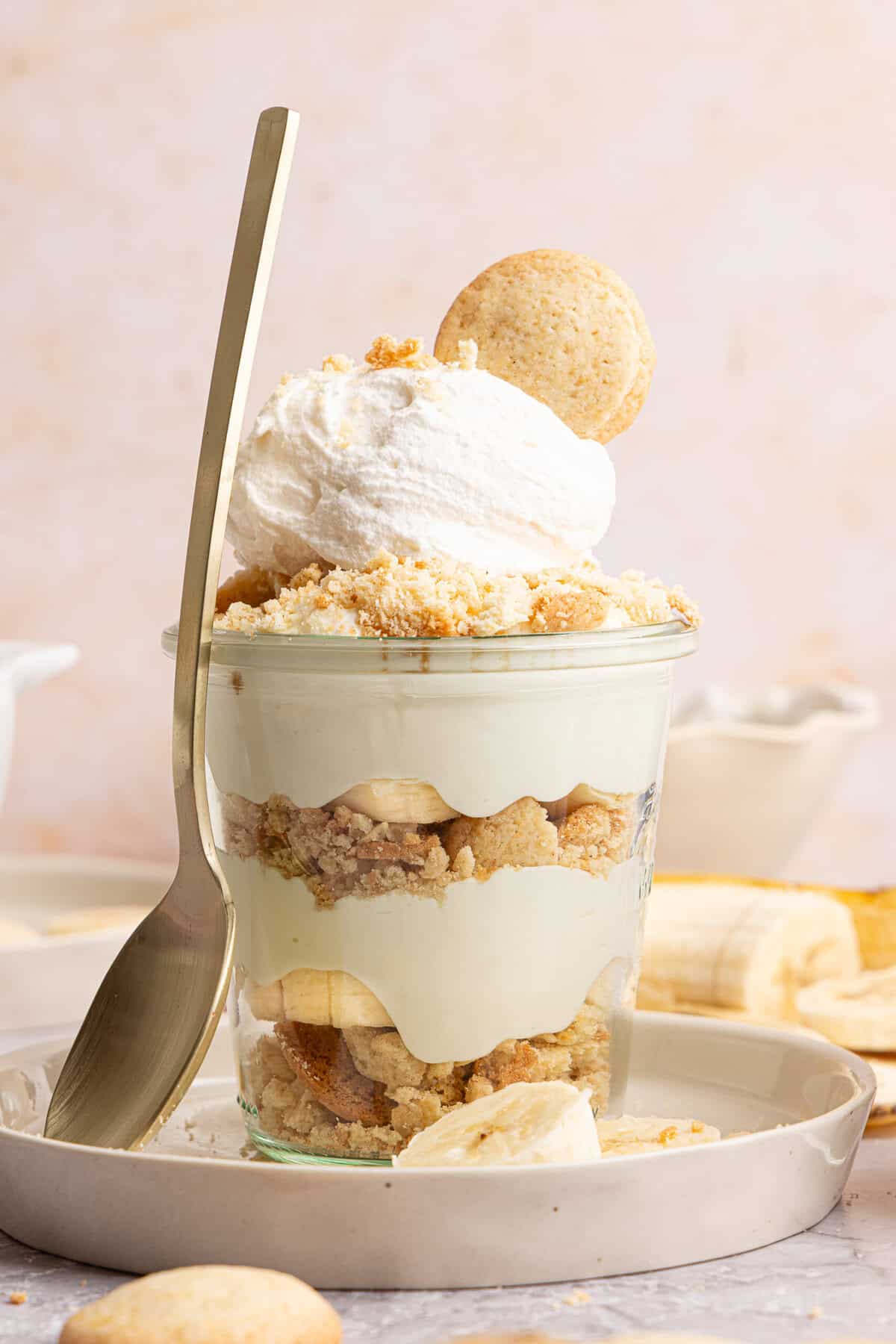 a banana pudding cup with a spoon rested against the side on a plate