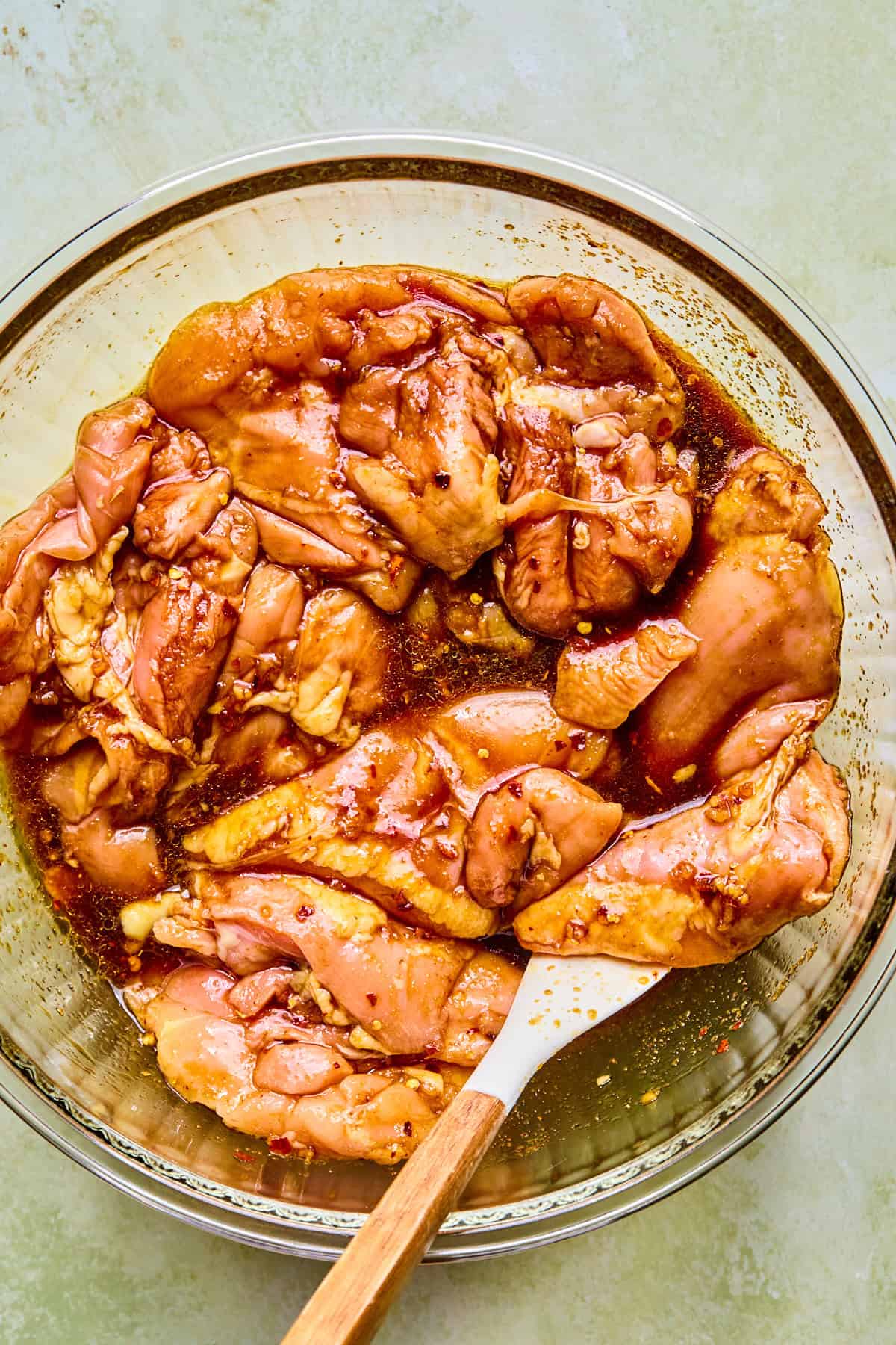Raw chicken thighs in a glass bowl coated with marinade.