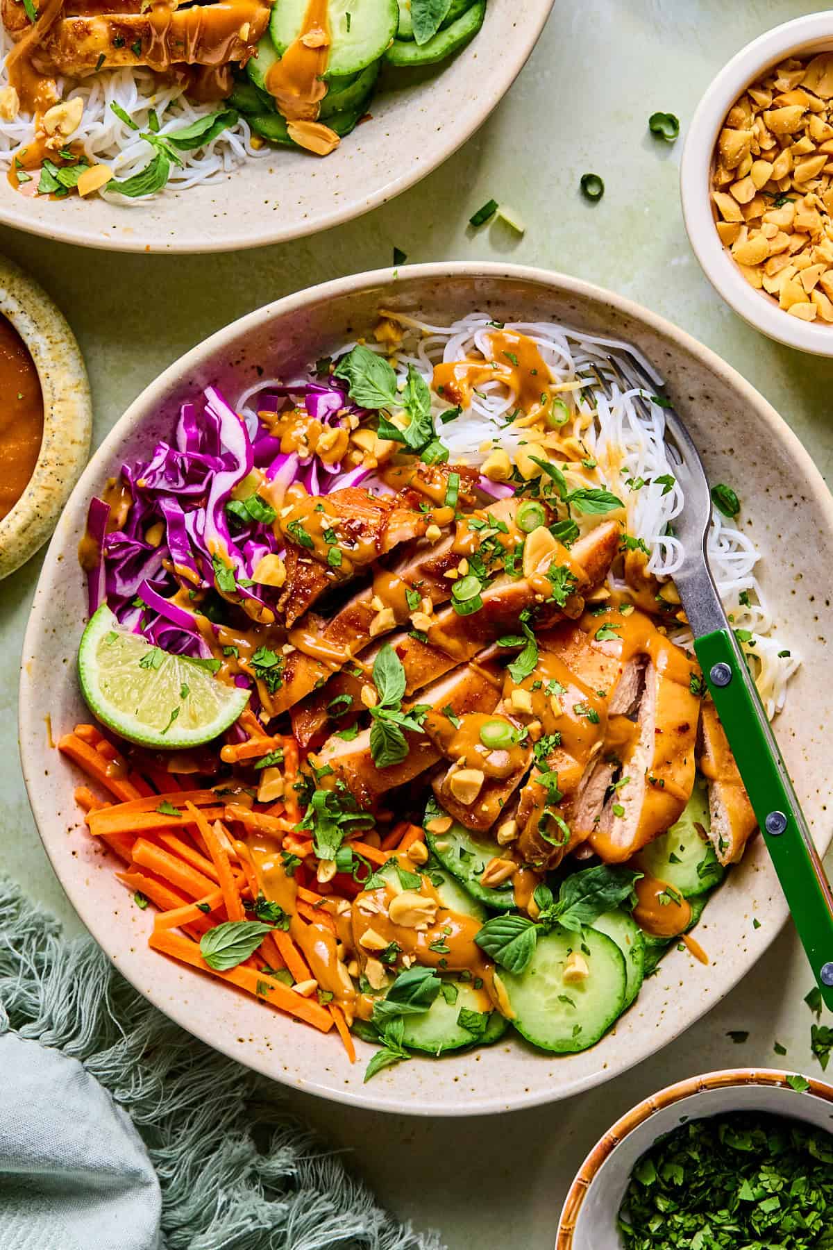Spring roll in a bowl topped with fresh basil and halved lime slices, with a fork resting inside the bowl.