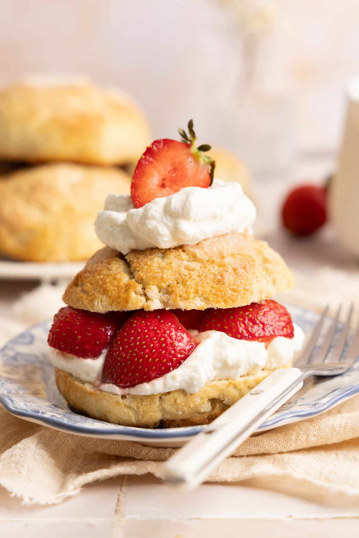 gluten free biscuit topped with strawberries and whipped cream on a plate with a white metal fork