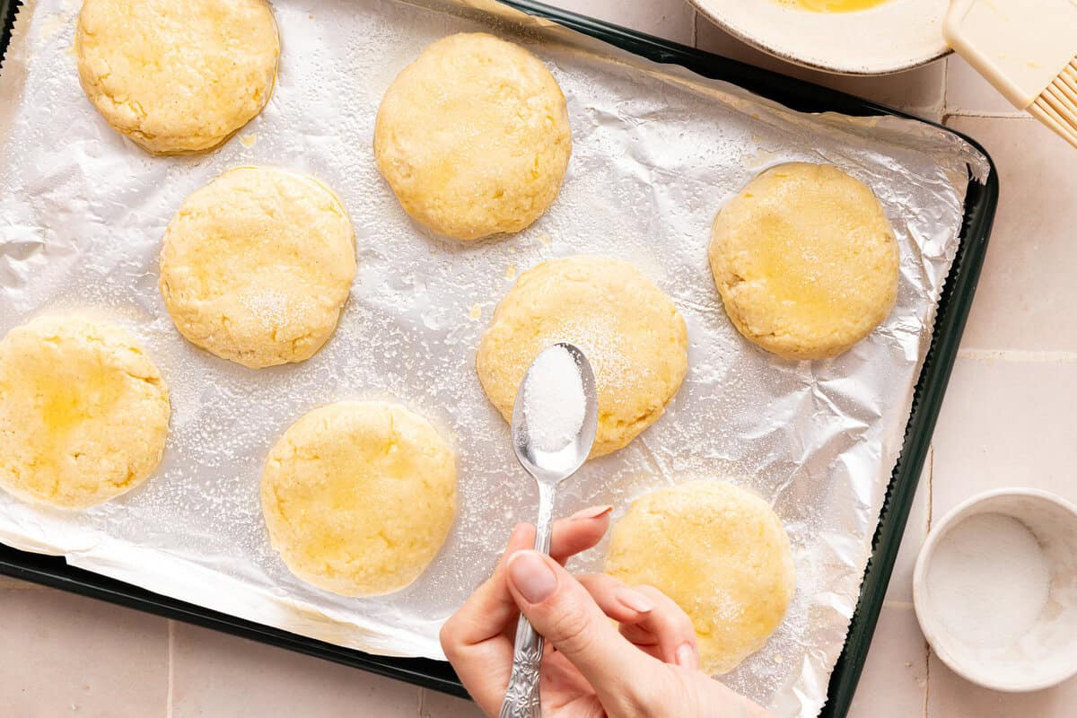 sugar being sprinkled on top of raw biscuits