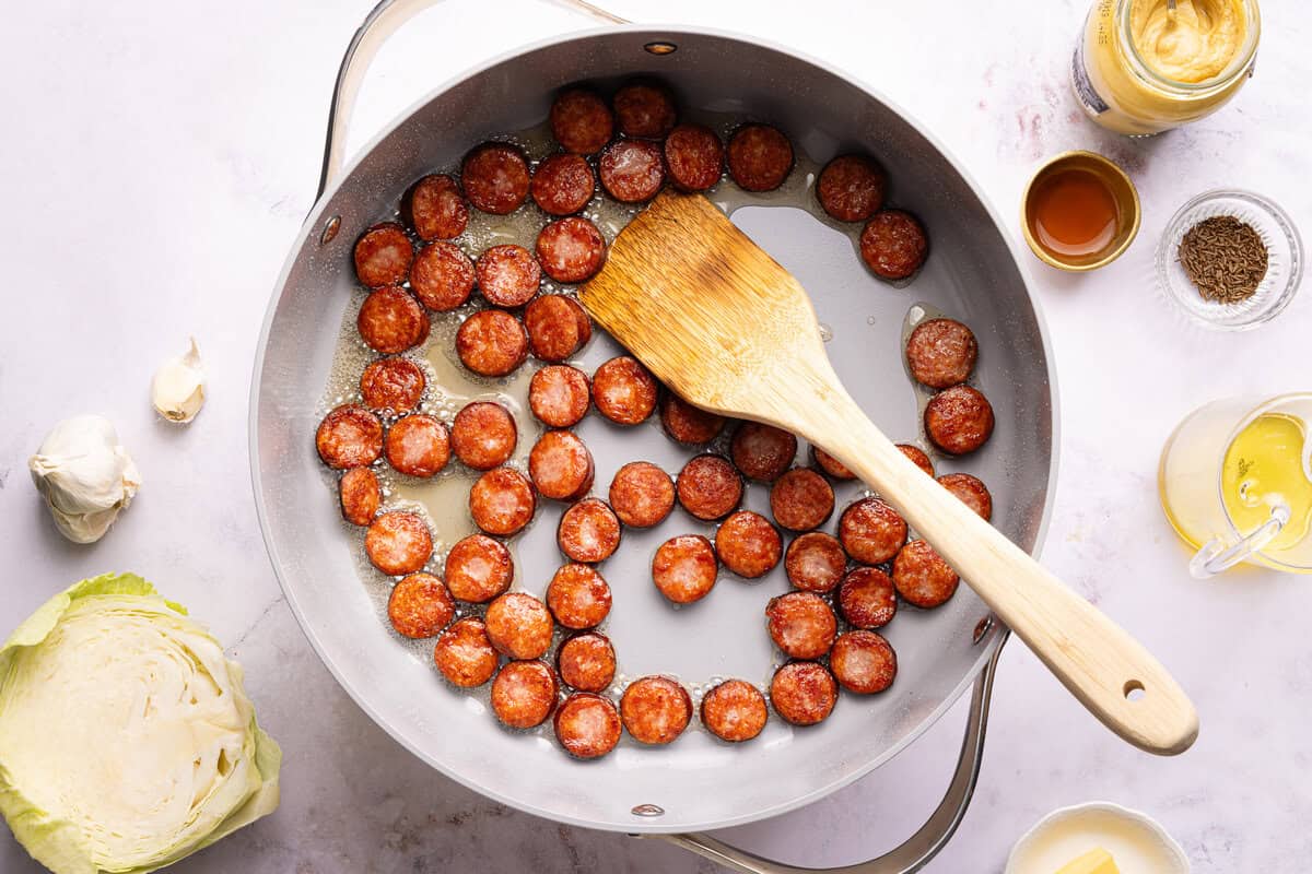sausage in a skillet with a wooden spoon