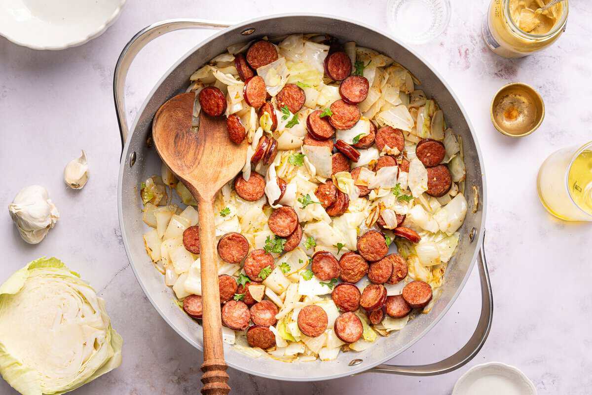 sausage and cabbage in a skillet with a wooden spoon