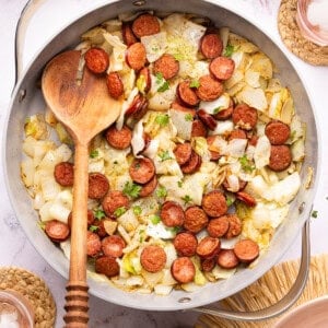 sausage and cabbage in a skillet with a wooden spoon