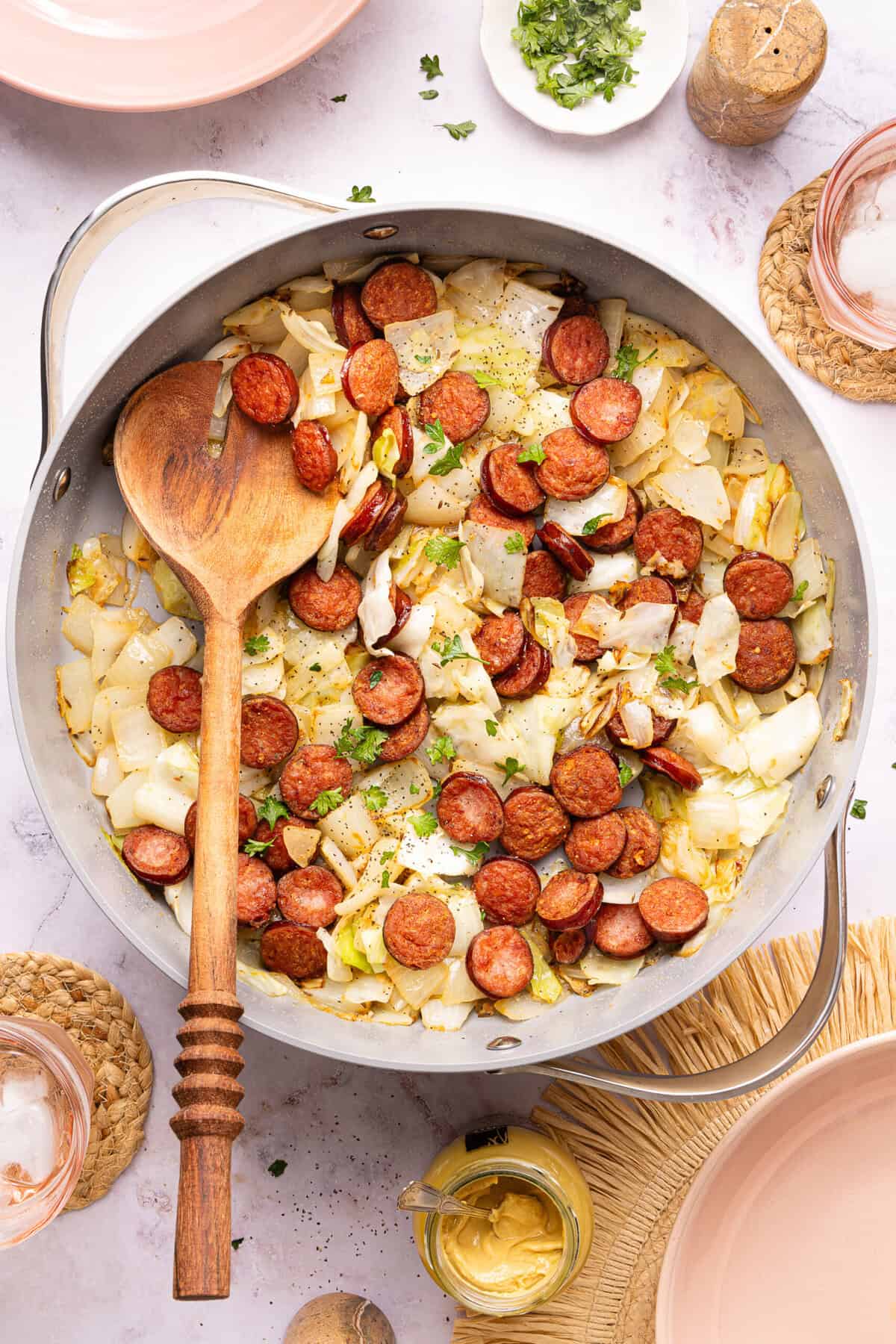 sausage and cabbage in a skillet with a wooden spoon
