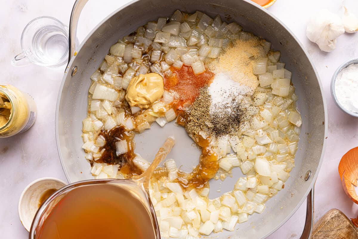 onions and spices in a pan with broth being poured in