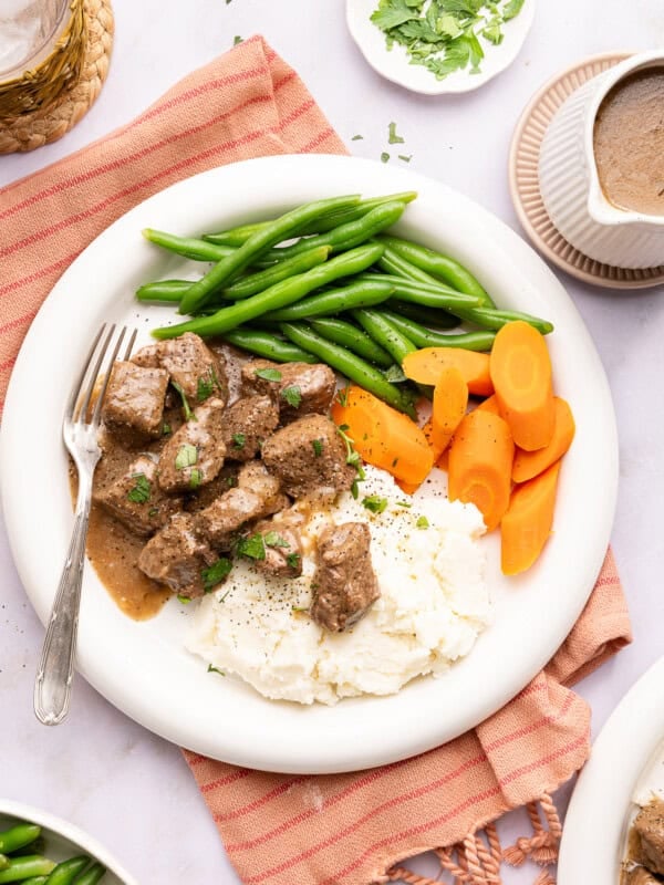 beef tips over mashed potatoes with green beans and carrots on a plate