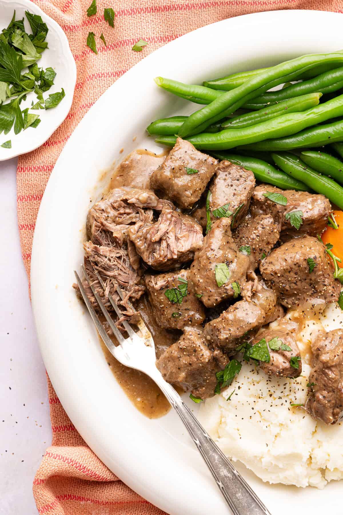 beef tips with gravy over mashed potatoes with green beans on a plate