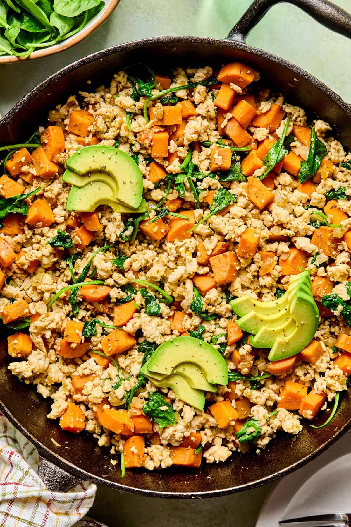 turkey sweet potato hash topped with avocado in a cast iron skillet
