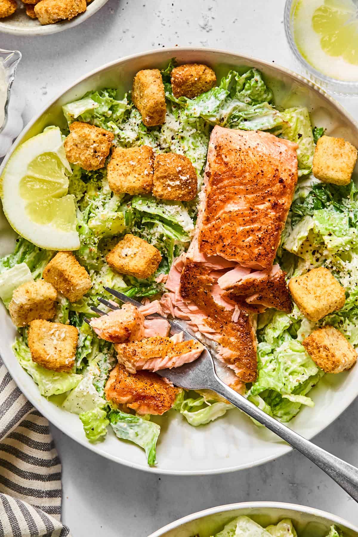 salmon caesar salad in a white bowl with a fork flaking some of the salmon apart