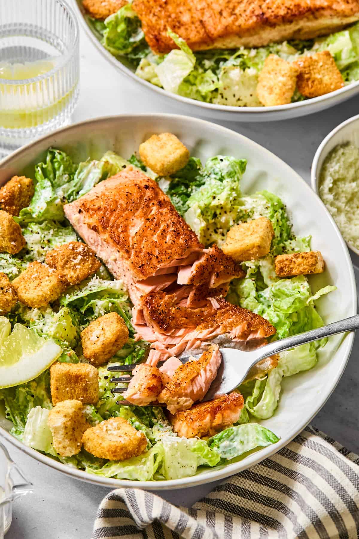 a side view of salmon caesar salad with a fork breaking apart the salmon