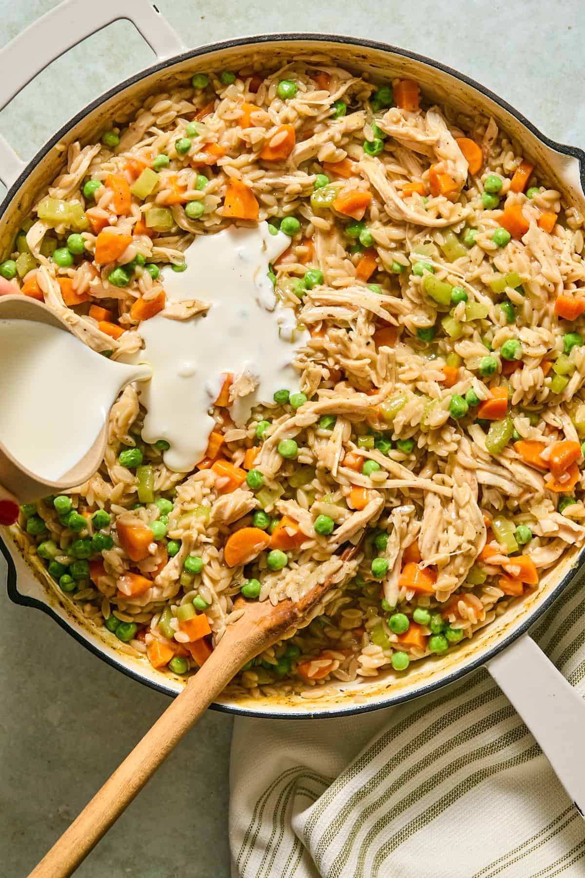 Half-and-half being stirred into the chicken and orzo mixture, creating a thick and creamy pot pie texture.