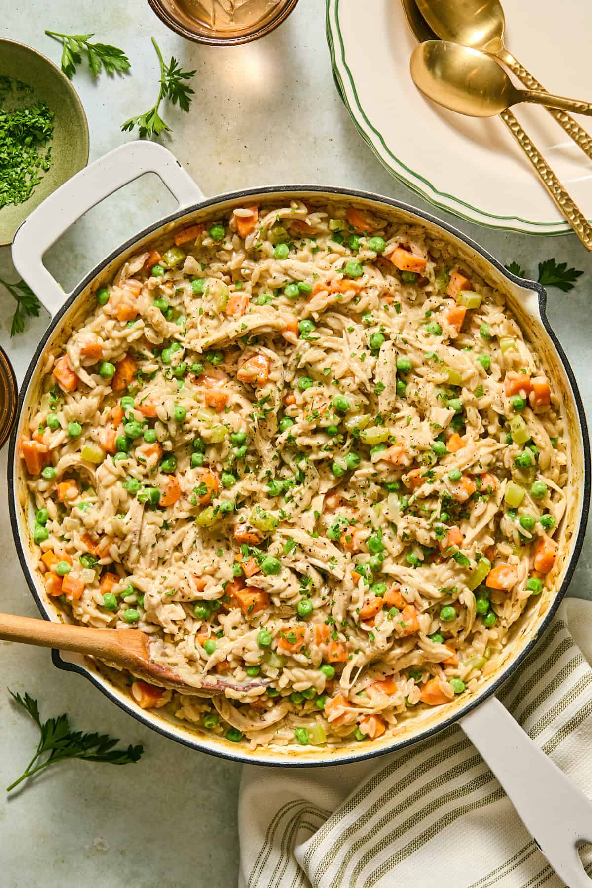 Chicken pot pie orzo in a large skillet with a wooden serving spoon in it.