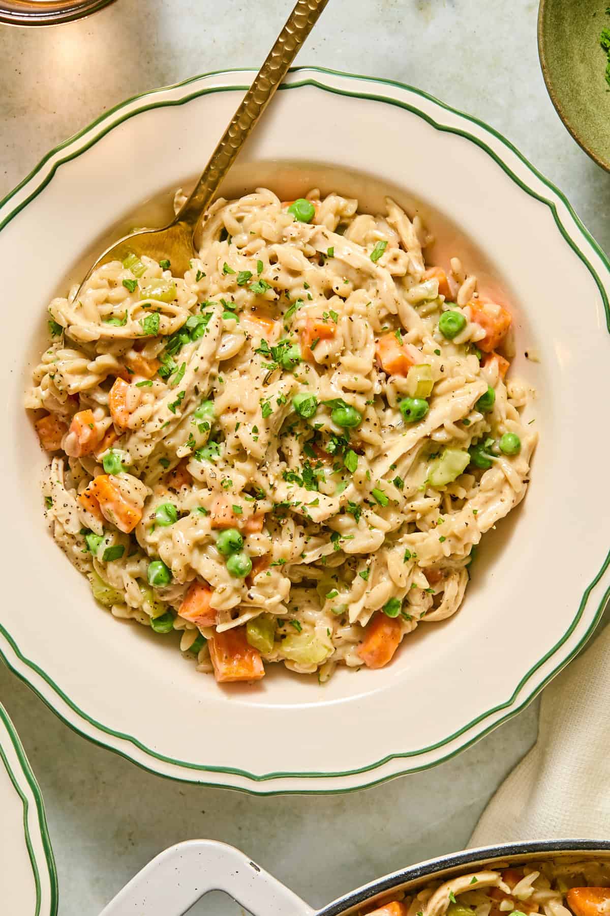 An overhead shot of a bowl filled with chicken pot pie orzo with a spoon in it.