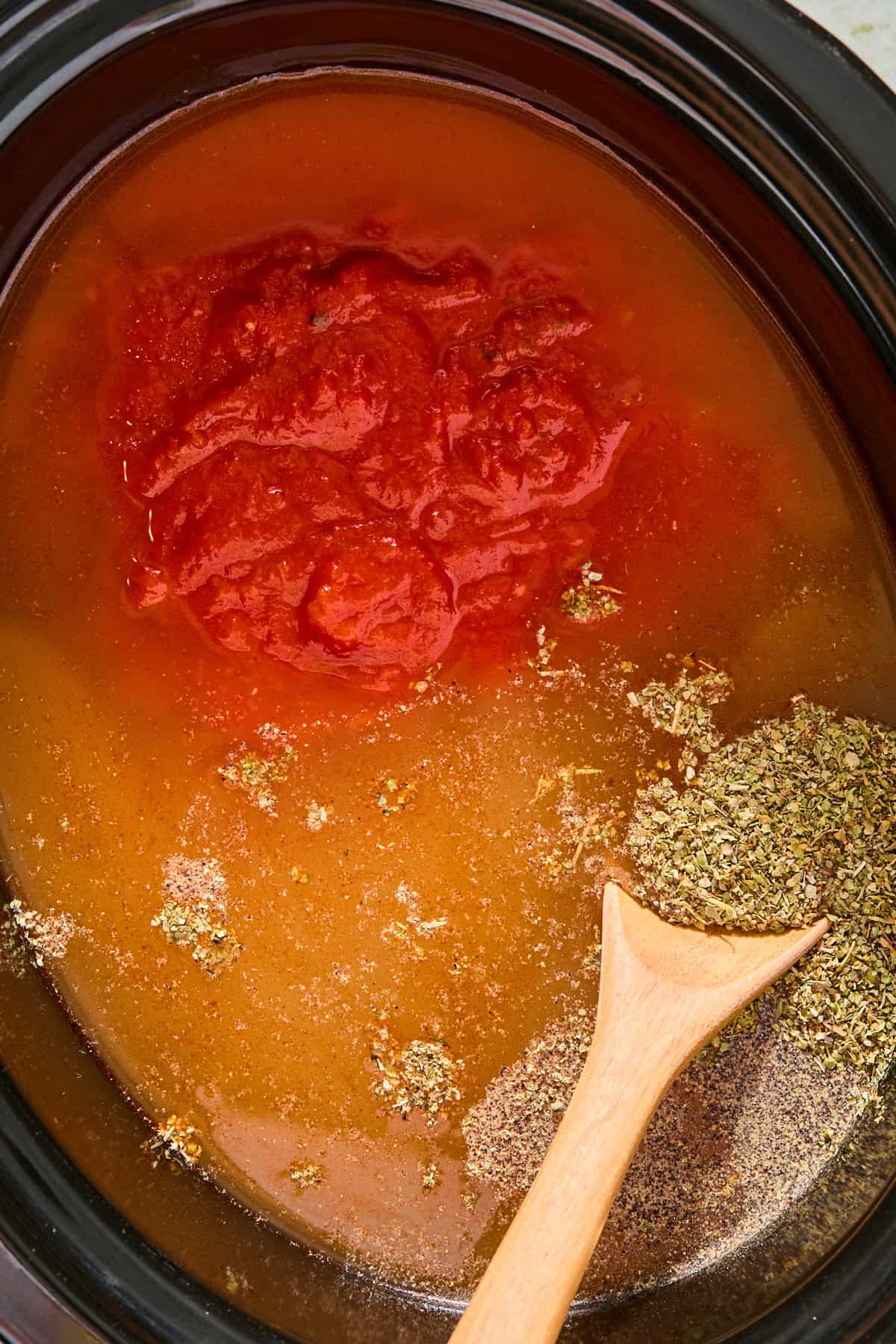 Raw chicken breasts, marinara sauce, and chicken broth in a slow cooker before cooking.