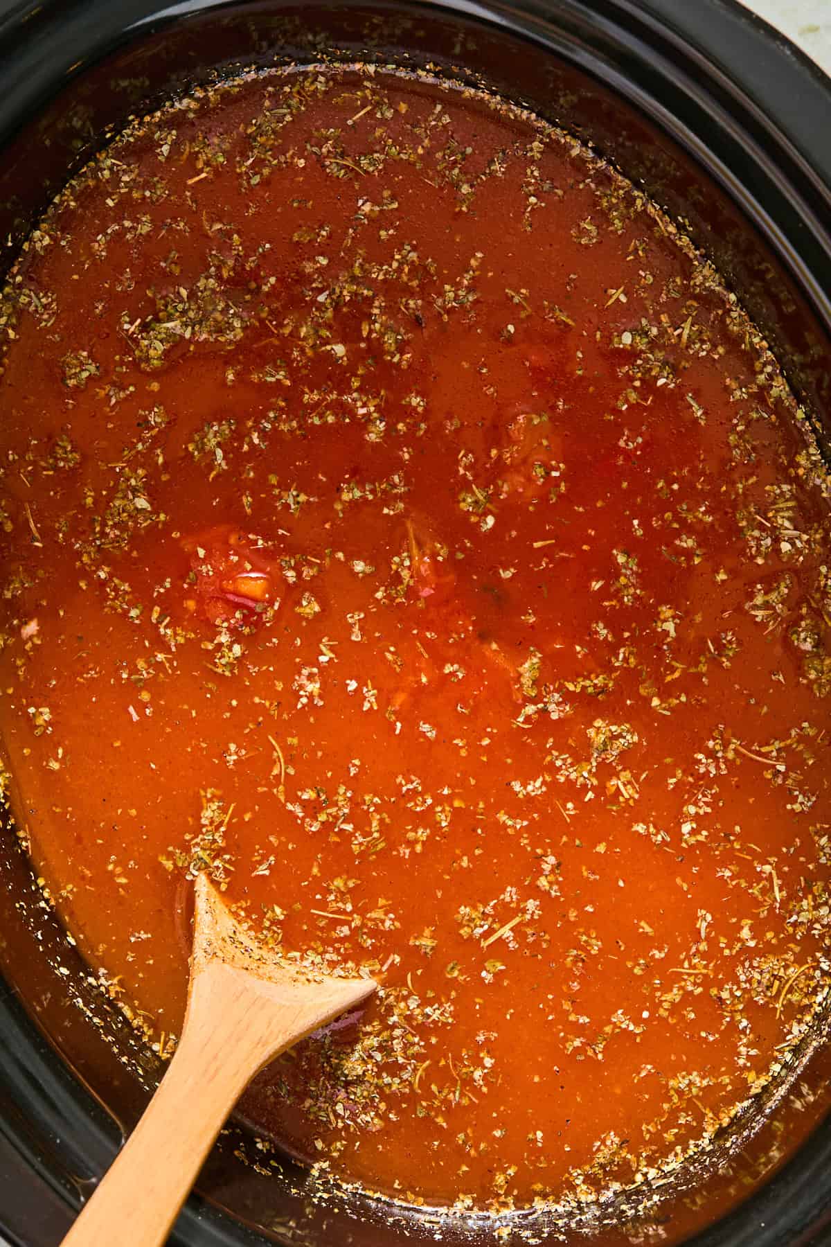 Raw chicken breasts, marinara sauce, and chicken broth in a slow cooker cooking.