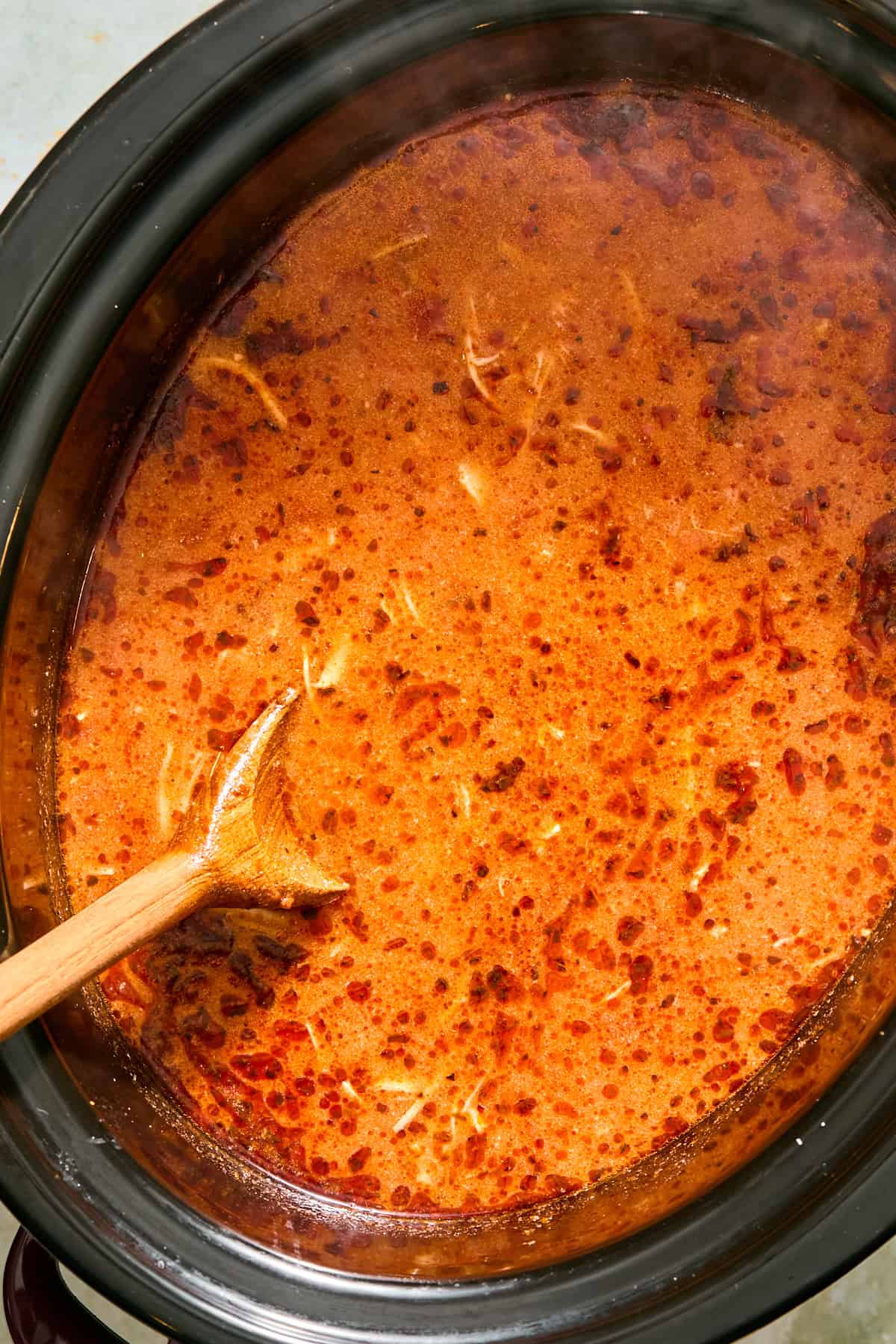 Uncooked gluten free fusilli being added to tomato chicken soup in a slow cooker