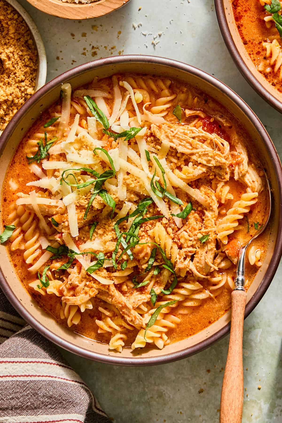Bowl of slow cooker chicken parmesan soup with shredded chicken and fusilli, topped with toasted panko, mozzarella, and fresh basil