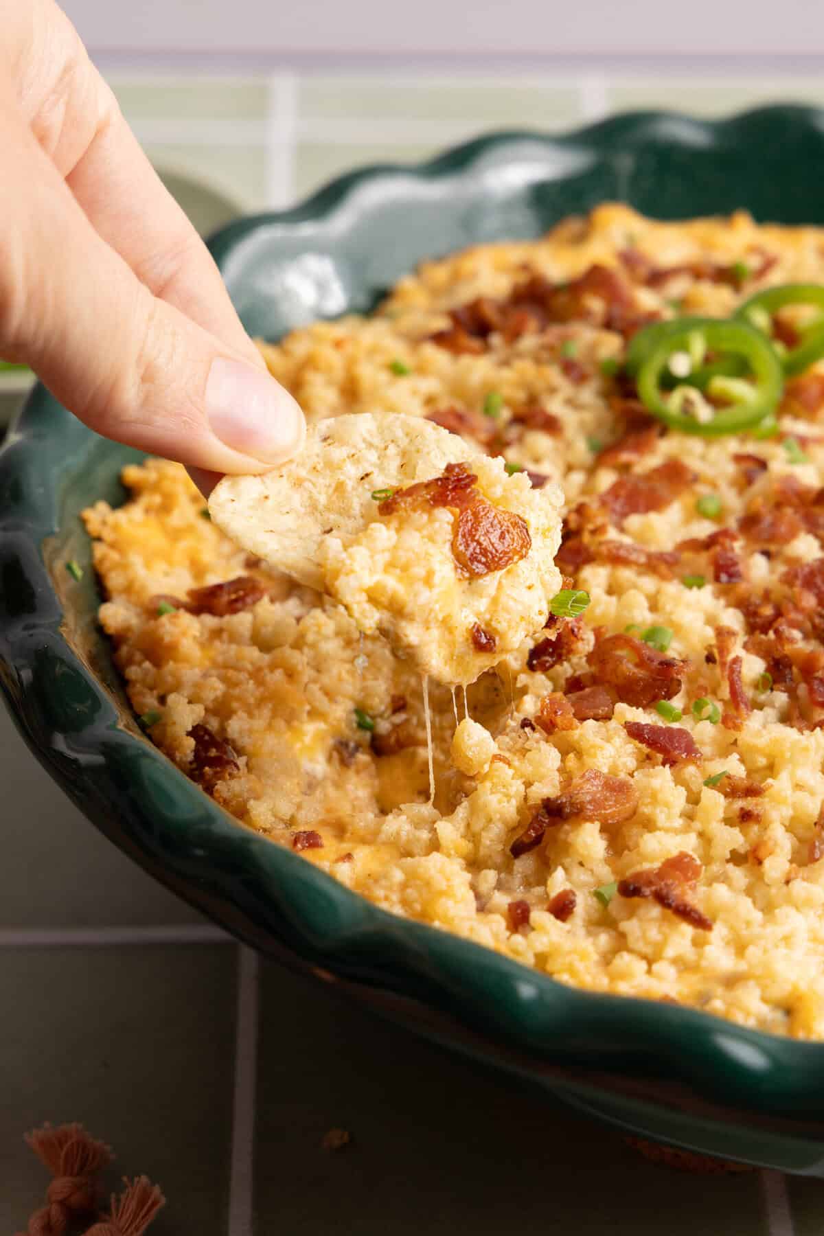a hand scooping out a scoop of jalapeño popper dip with a tortilla chip.