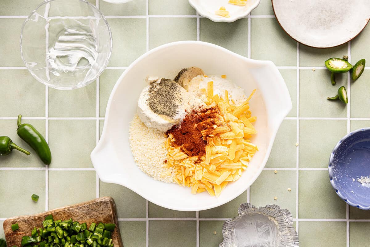 Cream cheese, Boursin, Greek yogurt, shredded cheddar, and seasonings being mixed in a white bowl