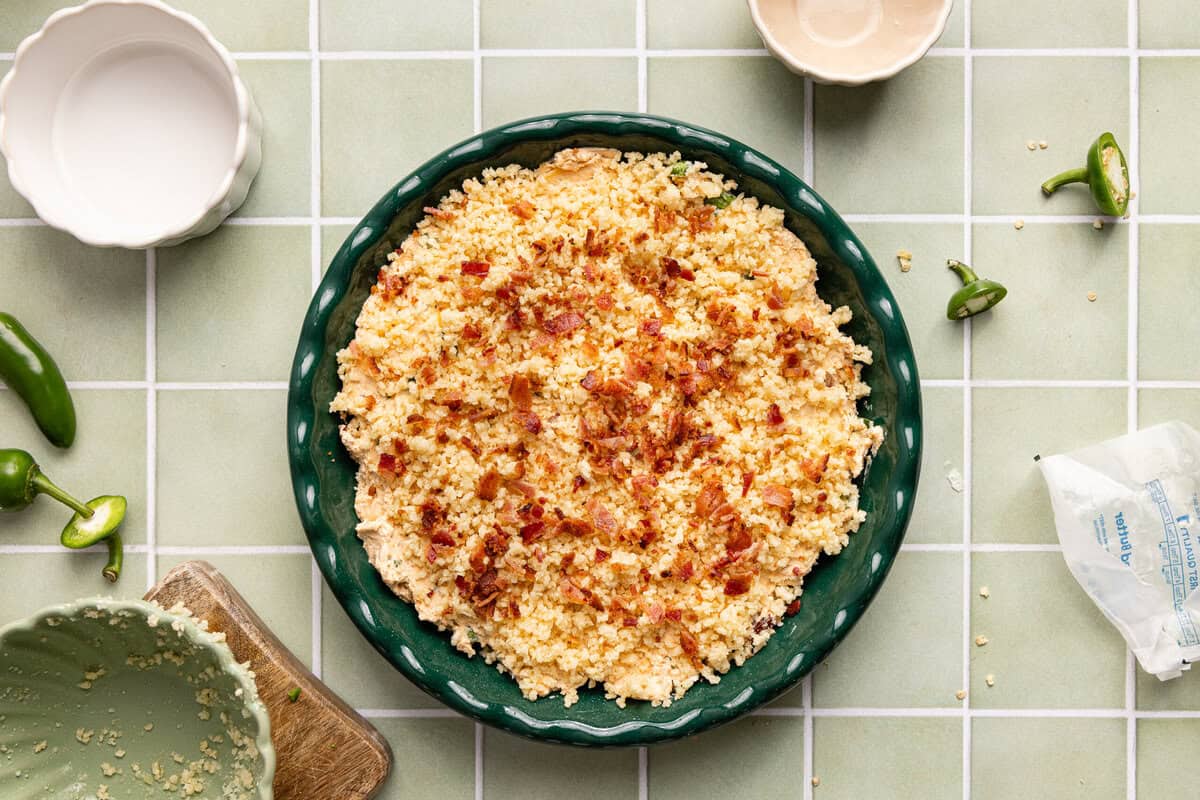 A round dish filled with jalapeño popper dip topped with gluten free panko, parmesan, and crumbled bacon