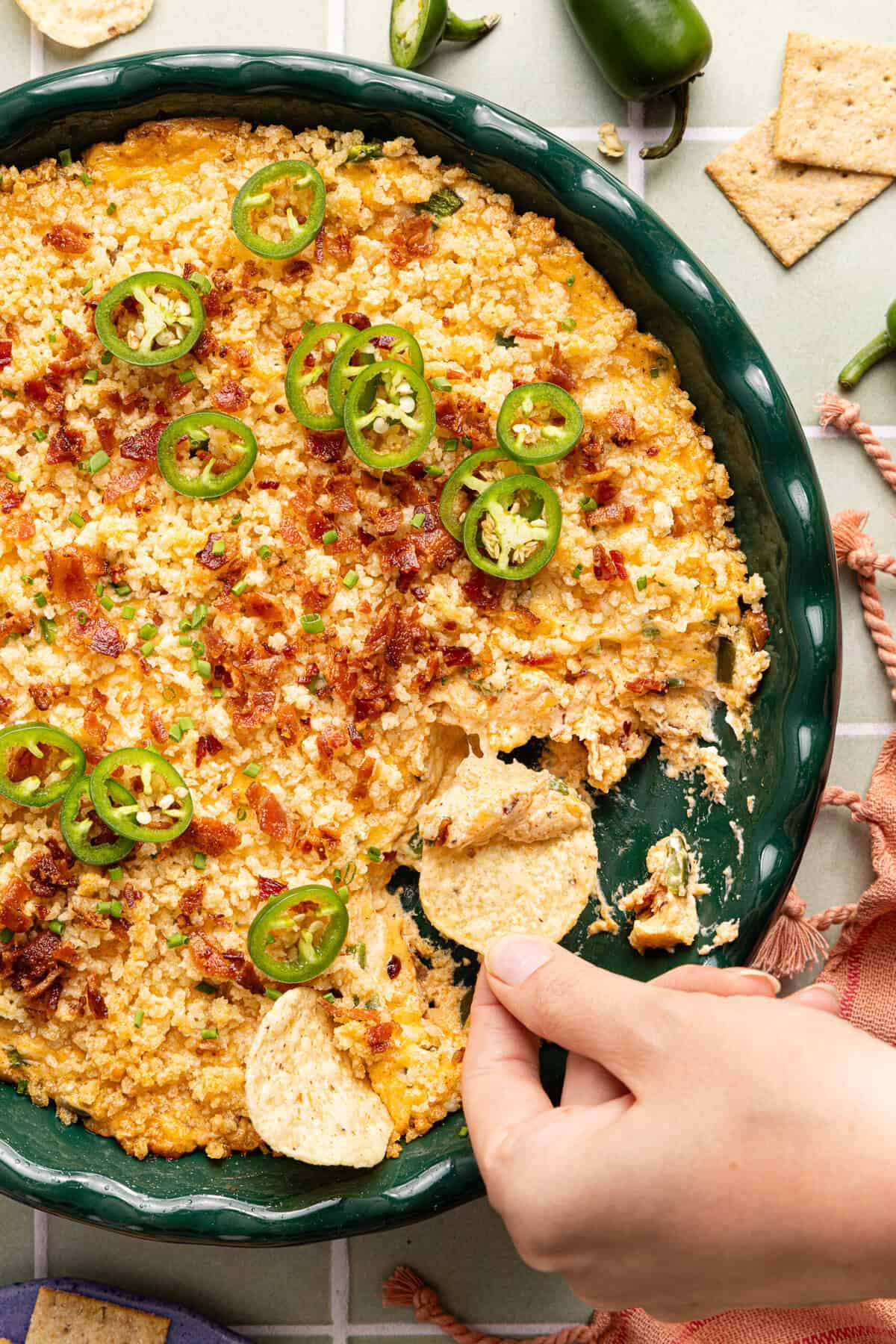 Baked jalapeno popper dip in a round dish with a golden panko topping, chopped chives, and a tortilla chip scooping from the corner