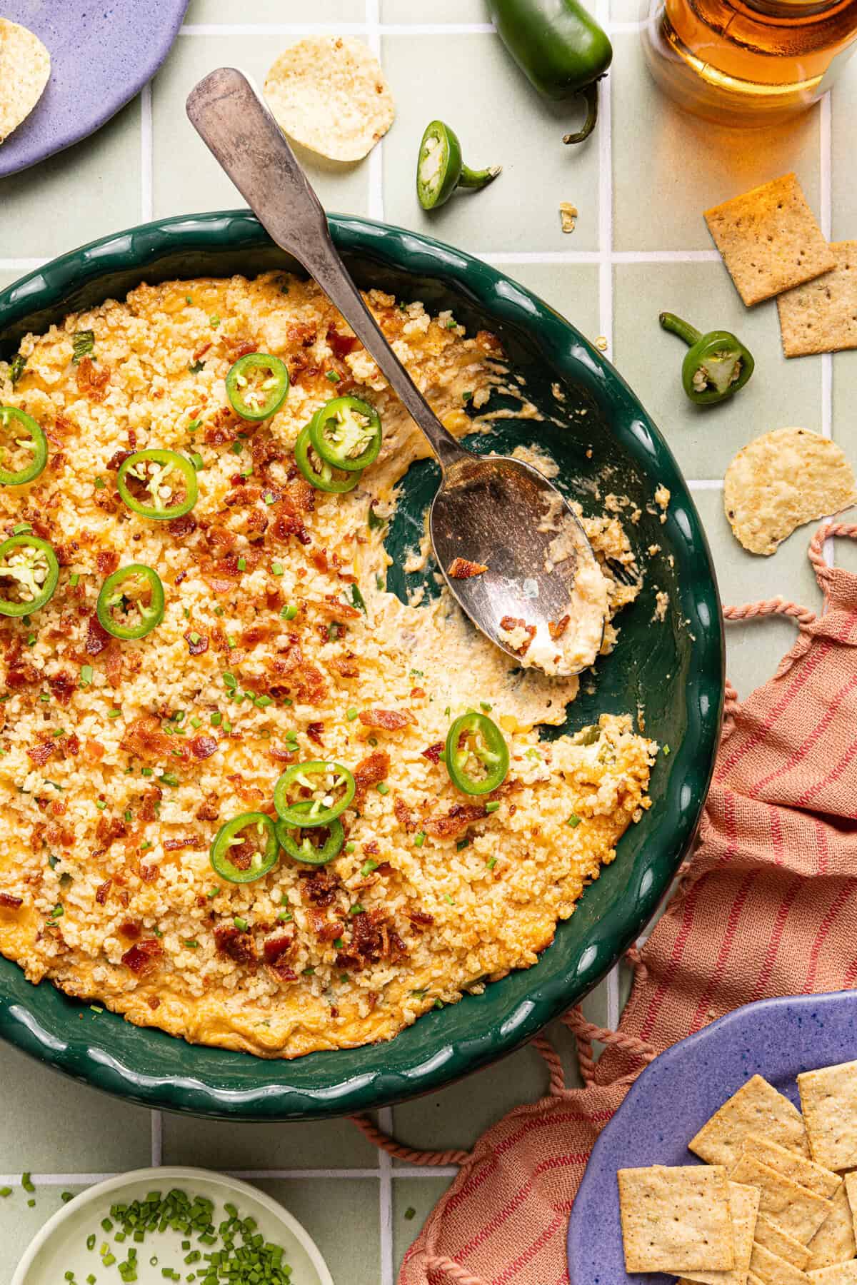 Half eaten jalapeno popper dip with a spoon resting inside the round green dish.
