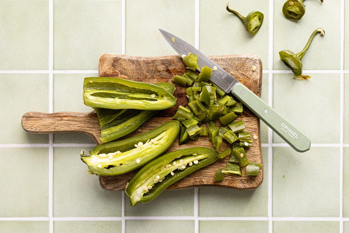 roasted jalapenos being chopped on a cutting board with a knife