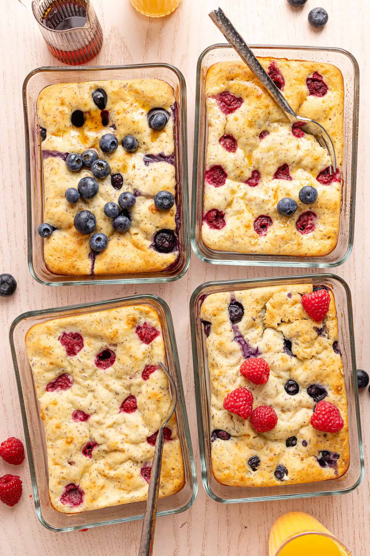 Four rectangular Pyrex glass containers filled with protein pancake bowls on a light wood countertop, with forks in two of the containers.