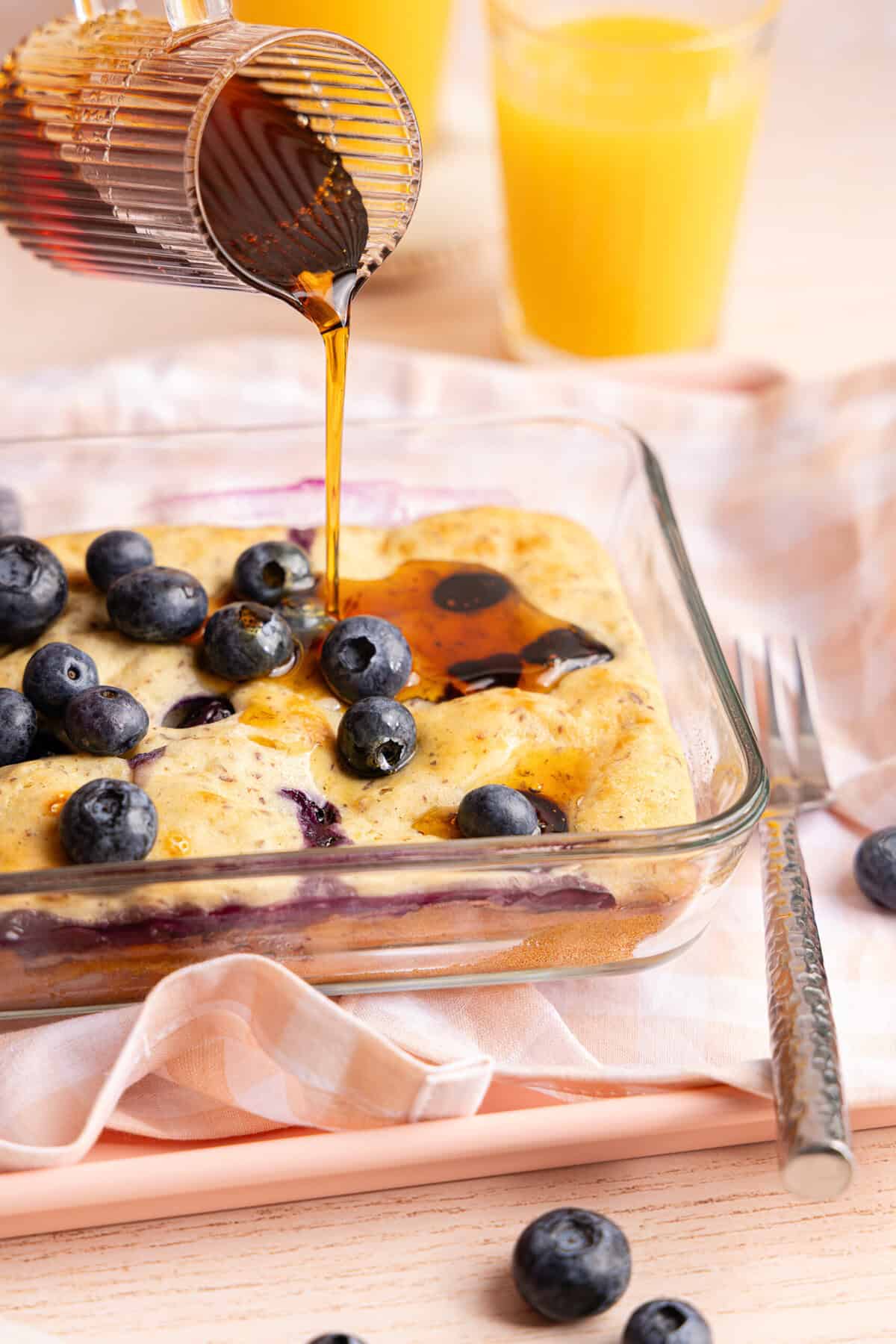 Close-up of syrup being poured over a blueberry protein pancake bowl.