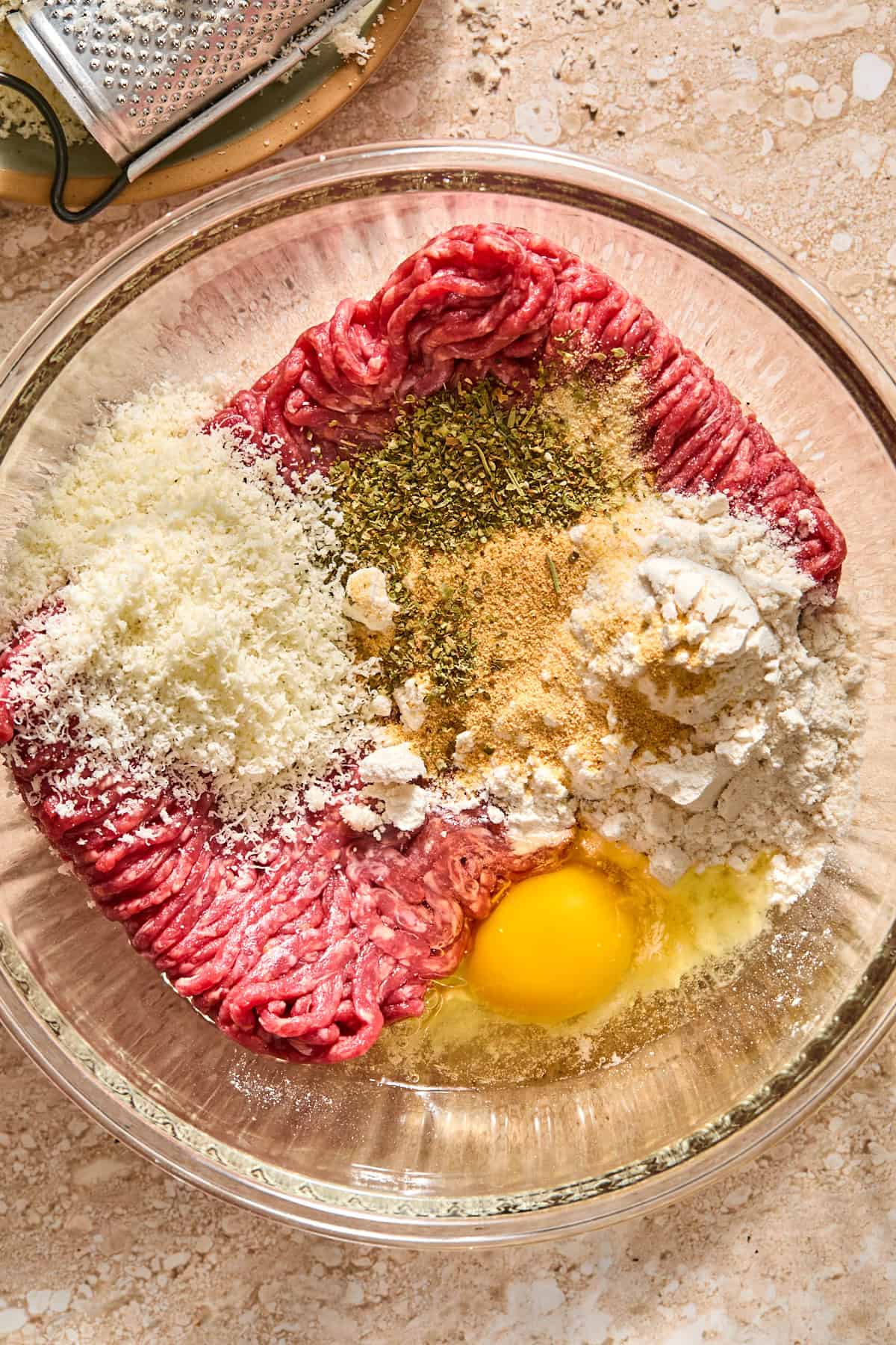 A glass bowl with all the ingredients to make meatballs before combining.