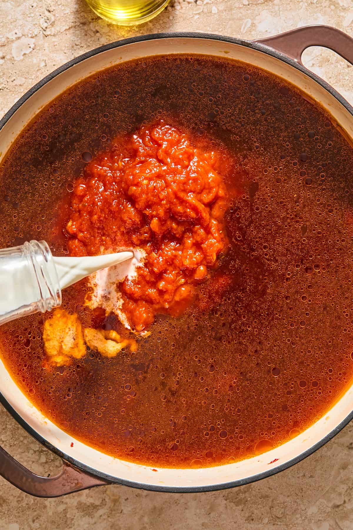 Pouring broth, marinara, and half and half into the pan with the tomato paste to form the sauce.