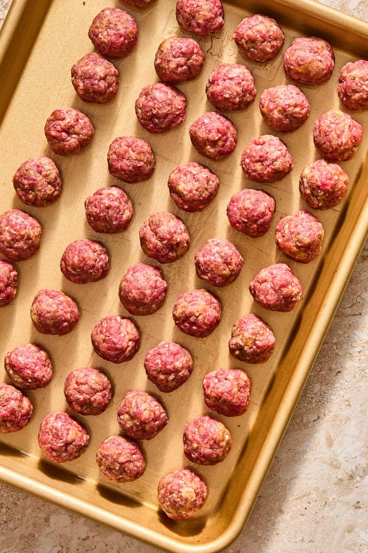 Raw mini meatballs rolled and placed on a sheet pan.
