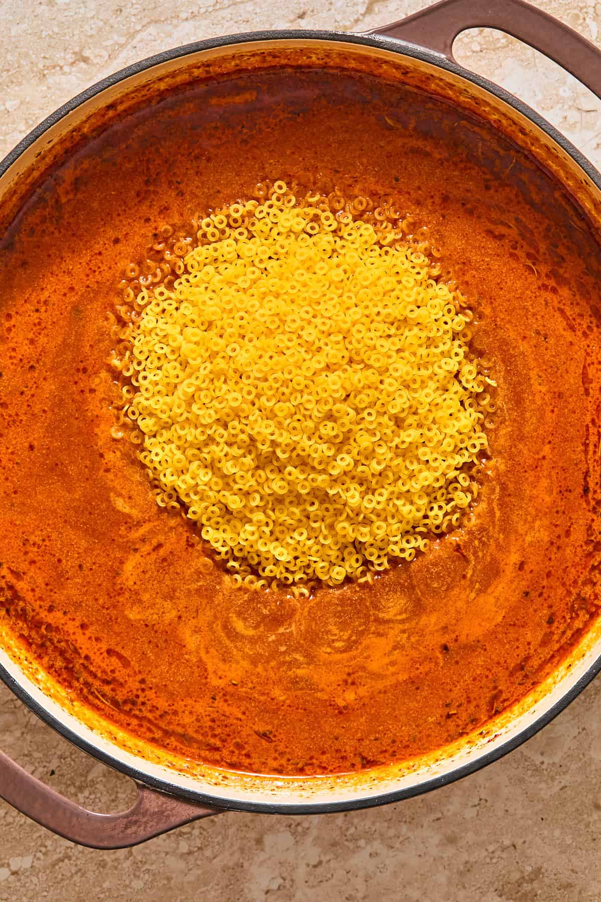 Uncooked, gluten free annelini pasta resting atop the pan of sauce.
