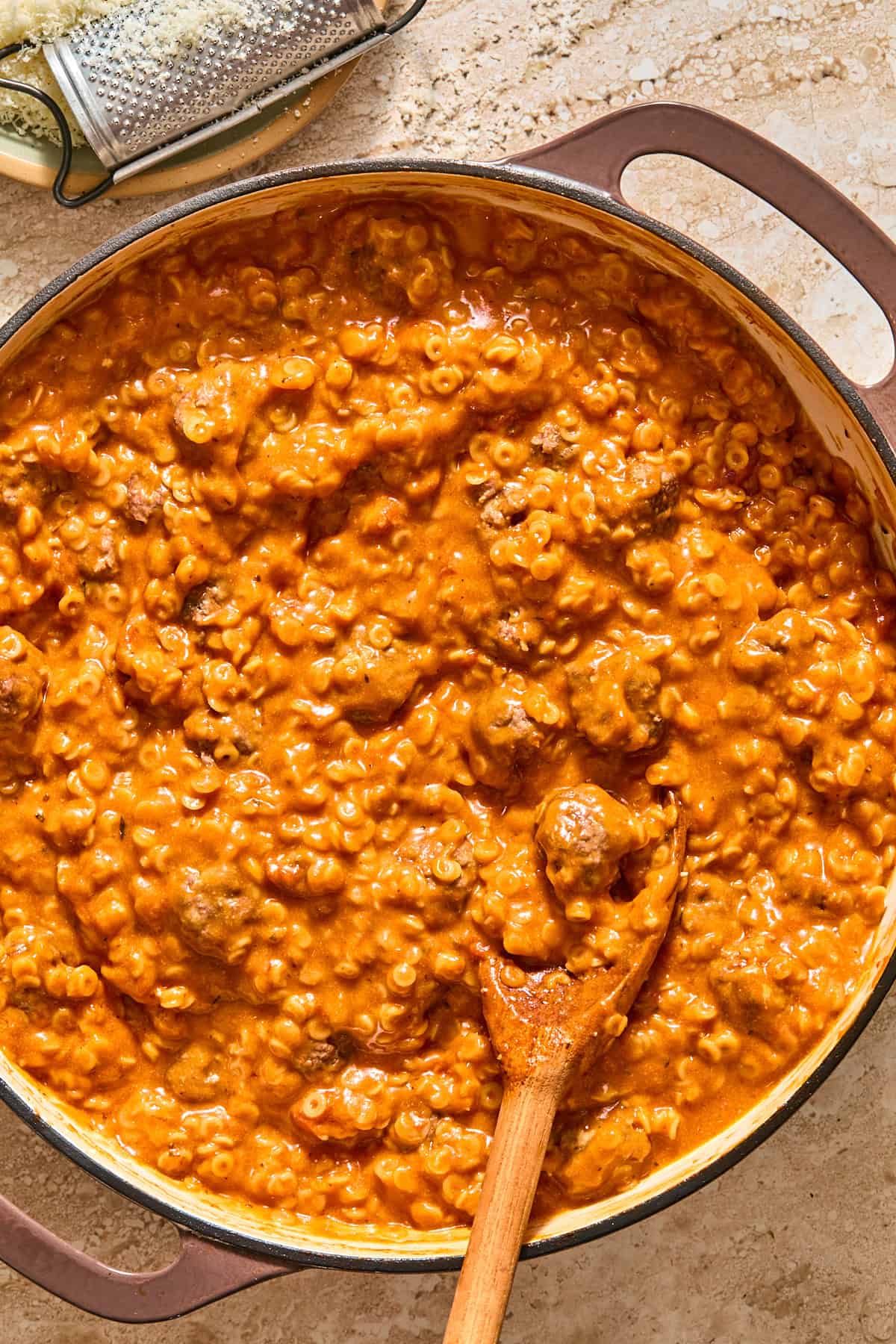 A close up of gluten-free spaghettiOs and mini meatballs getting stirred with a wooden spoon.