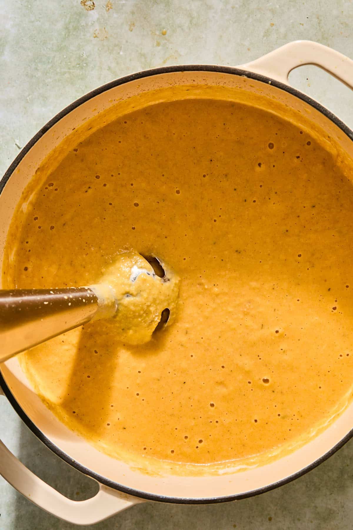 A creamy butternut squash soup getting blended with an immersion blender.